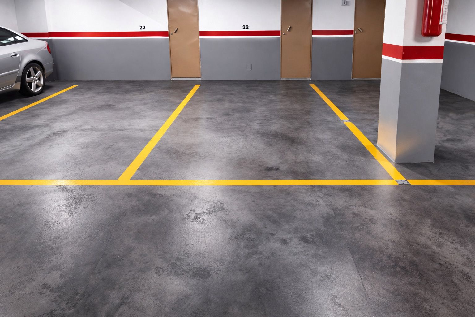 Garaje subterráneo pavimentado con mortero autonivelante de alta resistencia, con plazas numeradas delimitadas por líneas amarillas.